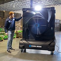 Man in navy jacket and jeans in a warehouse with his hand up on a large Cool Boss Industrial fan