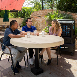 Two men and a woman sitting outside at a round table with water glasses on top, a medium sized Cool Boss fan is on behind the group